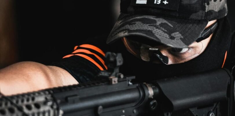 A soldier in camouflage uniform aiming a gun in a tactical setting, showcasing focus and precision.