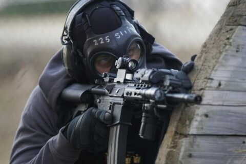 A tactical soldier in full gear aiming a rifle during an operation outdoors.