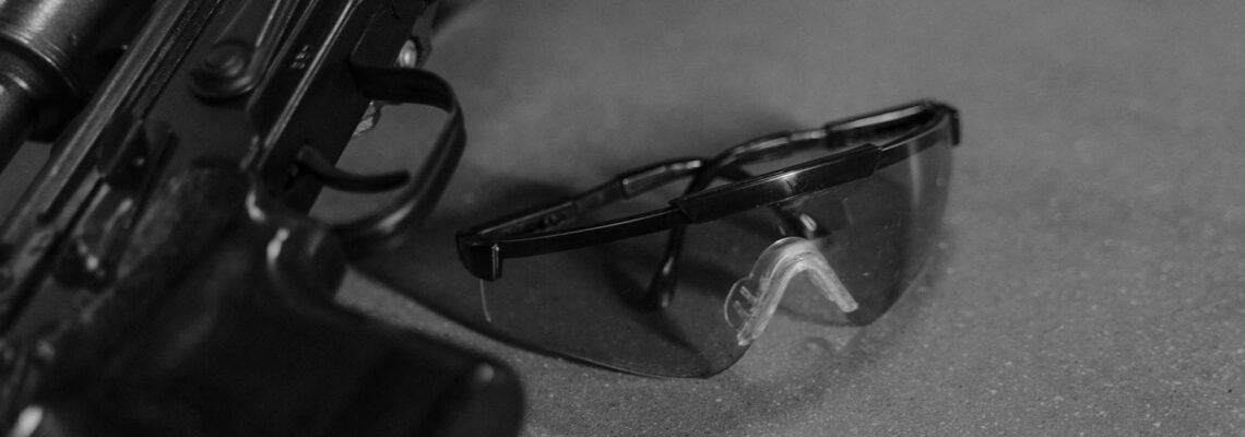 Detailed black and white photo of a rifle and safety glasses, highlighting firearm safety.