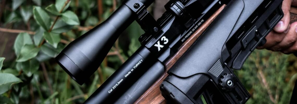 Detailed image of hands holding a scoped rifle against a natural background.