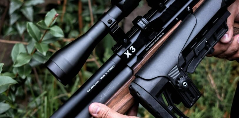 Detailed image of hands holding a scoped rifle against a natural background.